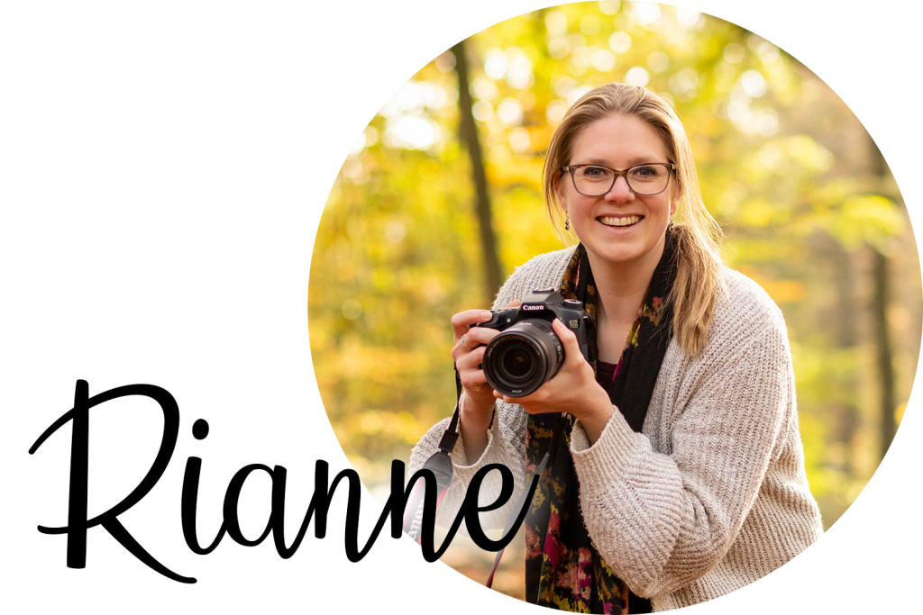 Foto van Rianne met een camera in haar hand. Ze lacht vrolijk en staat in het bos. 